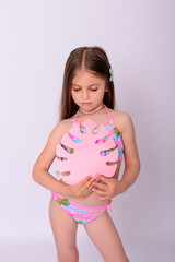 Cute little girl in bright swimwear holding pink tropical paper monstera leaf on white background © Alla