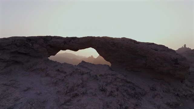 Stunning aerial view of the Ventana del Nublo, a natural stone arch, with Roque Nublo visible through it during a beautiful sunset
