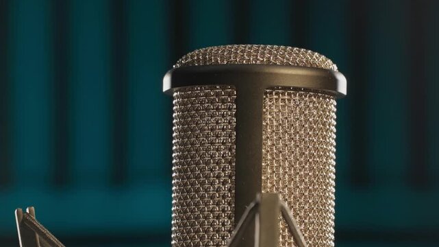 Slow motion colorful studio shot of voiceover dialogue podcast microphone on stand in close-up detail with acoustic foam in recording space with dark background and bright lighting of broadcast vo mic