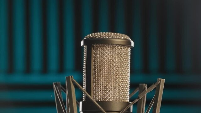 Slow motion colorful studio shot of voiceover dialogue podcast microphone on stand in close-up detail with acoustic foam in recording space with dark background and bright lighting of broadcast vo mic
