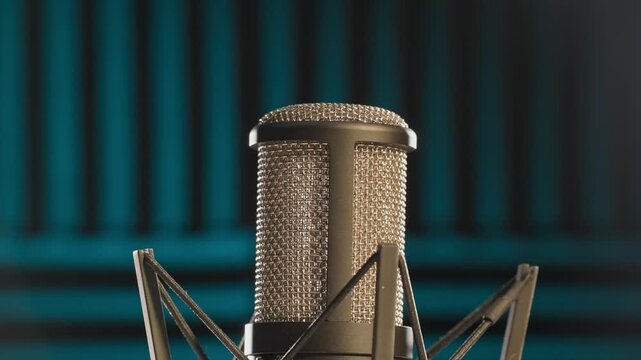 Slow motion colorful studio shot of voiceover dialogue podcast microphone on stand in close-up detail with acoustic foam in recording space with dark background and bright lighting of broadcast vo mic