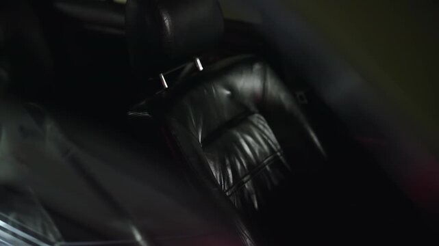 Luxury car interior showing an empty black leather passenger seat in a dramatic, dark, and moody setting, with a slow and smooth camera movement capturing the elegant and comfortable design