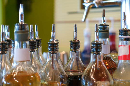 Nahaufnahme verschiedener Spirituosenflaschen und Barutensilien mit Ausgie&szlig;ern an einer Bar, Cocktailzubeh&ouml;r, mit einem Zapfhahn im Hintergrund, selektive Sch&auml;rfe und verschwommener Hintergrund