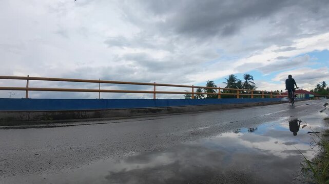 Slow Motion of Man Cycling on Wet Road Reflecting Sky