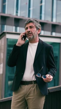 Video of happy mature businessman using smartphone while walking through the city.