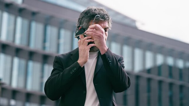 Video of happy mature businessman using smartphone while walking through the city.