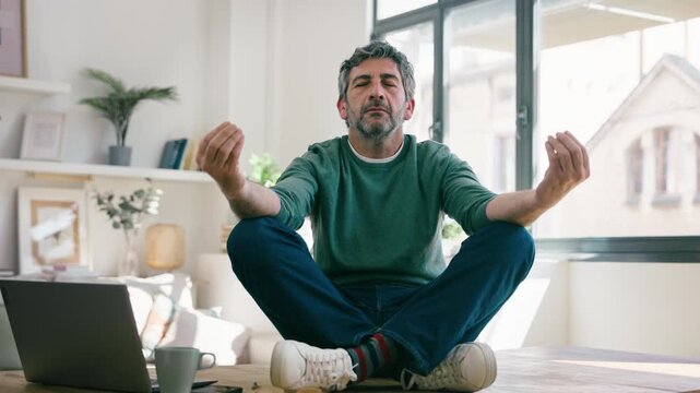 Video of mature man doing yoga stretches at his desk while working on a laptop at home