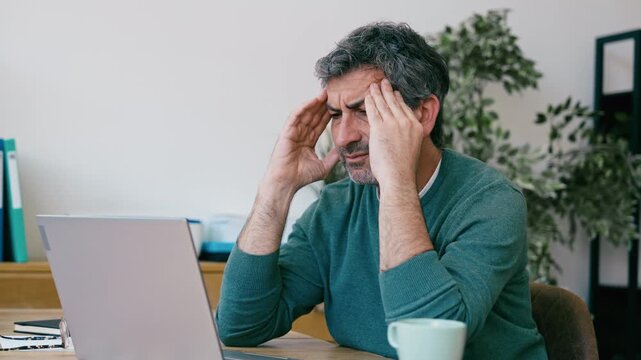 Video of tired man with headache working with laptop at the office