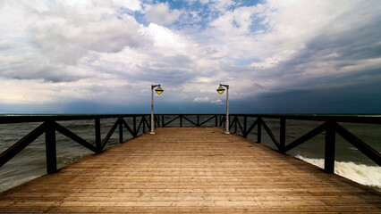 Fototapeta premium Wooden pier with lamps leading to the sea under a dramatic cloudy sky