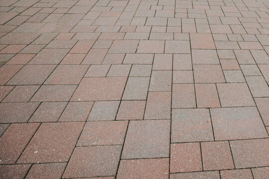 Close-up view of rectangular red and gray paving stones arranged in a varied interlocking pattern, creating a clean geometric background