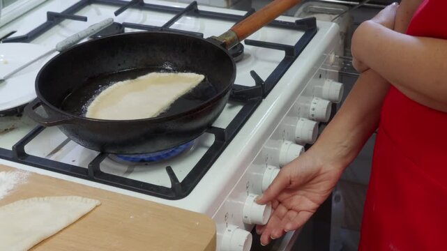 A focused cook carefully adjusts the gas stove knob while frying a fresh pastry in a hot pan. They work passionately inside a bright kitchen during a joyful meal routine.
