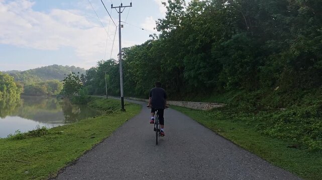 Slow Motion of Man Cycling Beside Lake on Paved Path