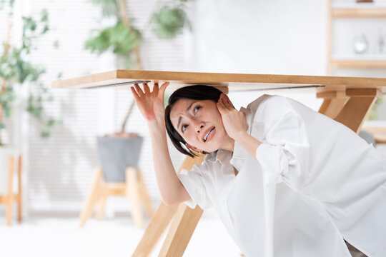 地震が起きてテーブルの下に隠れる女性