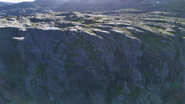 Drone aerial of rugged Trolltunga rock formation and surrounding mountains in summer sunlight, Norway.