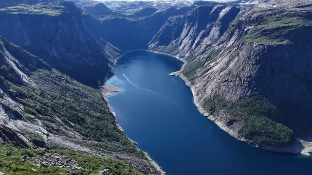 Drone panorama over deep blue water framed by steep rocky cliffs and forested slopes near Trolltunga, Norway.