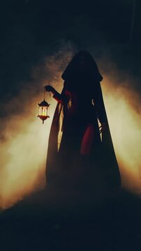 unrecognizable silhouette gothic woman ghost walking in dark dense fog forest hands hold lantern lamp illuminating way. long black dress cape hood. Fantasy girl princess. Night nature vertical video