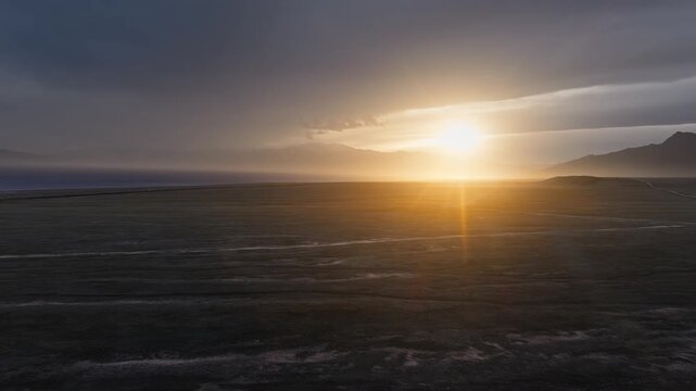 Golden sunset illuminating a vast desert landscape with distant mountain silhouettes under a stormy sky in Xinjiang.