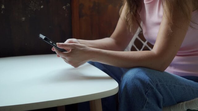 A calm woman holds a smartphone while sitting at a white table indoors. She feels relaxed and peaceful during a quiet moment of connection.