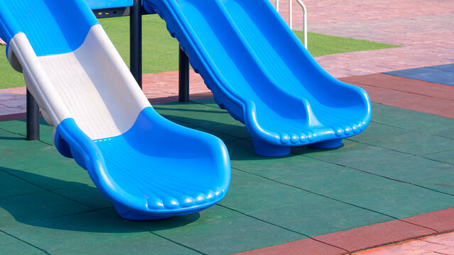 Blue and white plastic slides on colorful rubber safety tiles floor at outdoor playground in sunny day