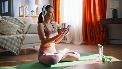 Fotobehang Lotusbloem Sporty asian girl browsing phone before yoga meditation. Lotus pose home mat.  © stockbusters
