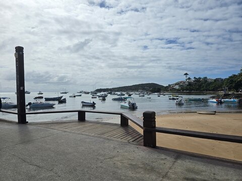 Scenic view of Orla Bardot boardwalk with boats floating in the calm bay under cloudy blue sky in Armacao dos Buzios, Rio de Janeiro, Brazil.