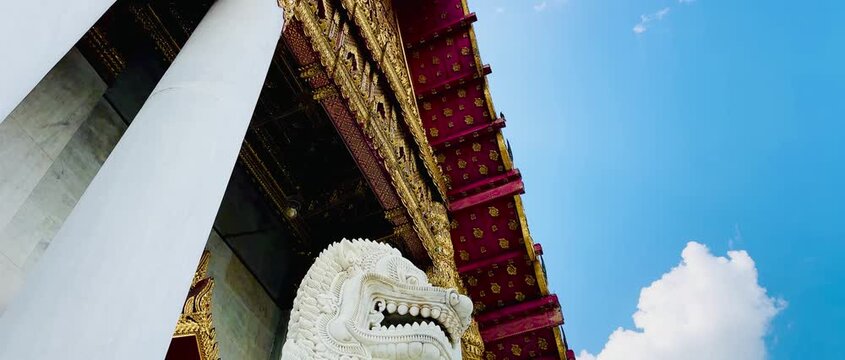 White marble guardian lion statue at the main hall entrance of Wat Benchamabophit in Bangkok, showcasing classical Thai architecture against a clear blue sky with white clouds.