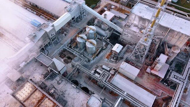 Intricate piping and tanks at a factory. An overhead aerial view displays a complex network of industrial pipes and metallic storage cylinders.