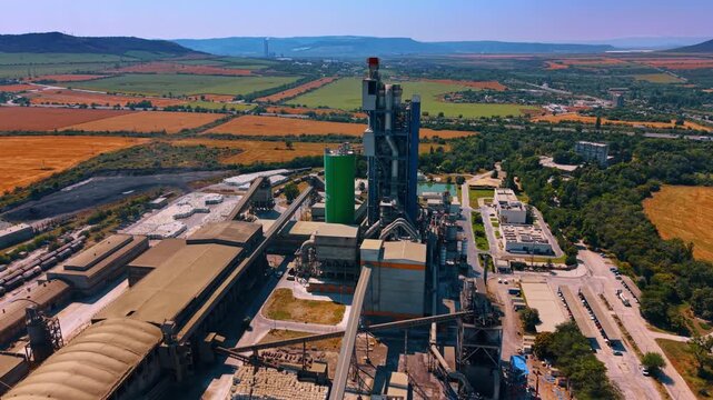 Modern industrial facility featuring a tall processing tower. A green silo stands prominently near the manufacturing structures under a clear sky.