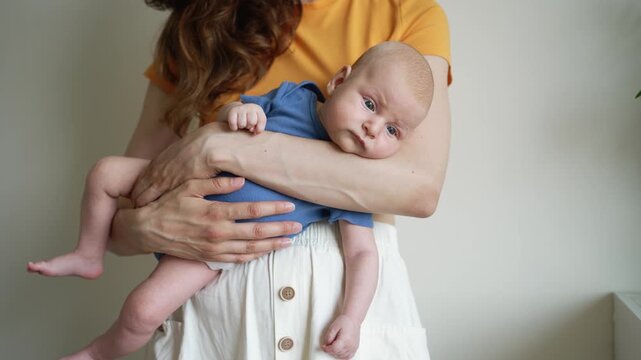 Loving mother gently holding her sweet newborn baby boy in her arms, beautiful moment of bonding between a new mom and her cute little son at home, concept of parenthood and happy family