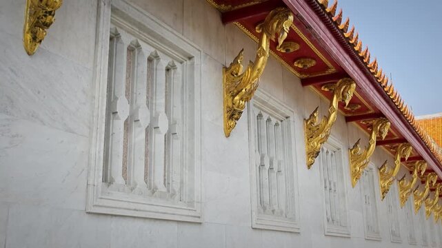 Ornate Gilded Eaves With Decorative Carvings On White Temple Exterior Wall