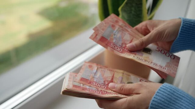 Close up of female hands carefully counting a thick stack of five thousand russian ruble bills, representing income, savings, financial accounting, and wealth management concepts