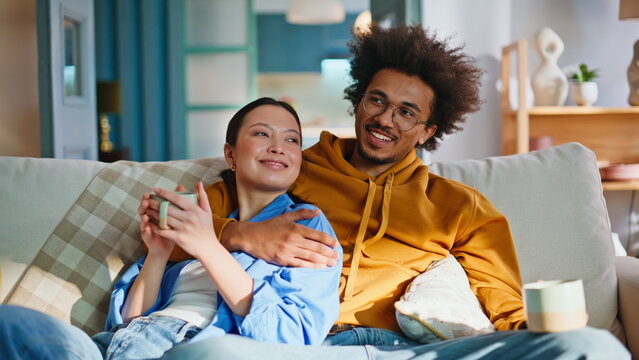 Interracial couple relaxing on sofa with coffee. Cozy weekend morning at home.