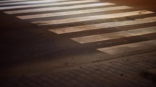 Nighttime scene of a zebra crosswalk with a car driving over painted road markings, emphasizing motion, urban traffic, pavement texture and pedestrian safety under low evening light, 4K