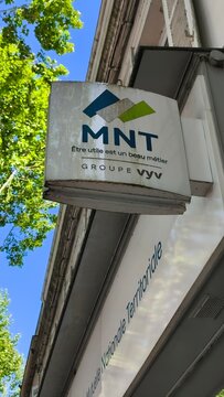 Saintes, France - April 21, 2026: Saintes. MNT signboard with logo and slogan visible on a building exterior under a clear blue sky in an urban setting