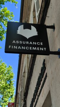 Saintes, France - April 21, 2026: Saintes. Assurance Financment sign mounted on a building exterior with green trees and blue sky visible in the background