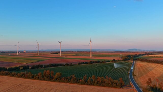 High angle view of wind turbines and road beside green field. An asphalt road borders an irrigated crop field beneath wind generators under a clear sky.