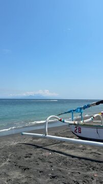 Traditional Balinese Jukung boat on black sand beach at ocean coast