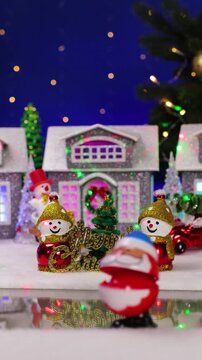 Ahead of a large Christmas town with snowmen with letters in the foreground, a yellow car drives by and an unusual Santa Claus jumps out