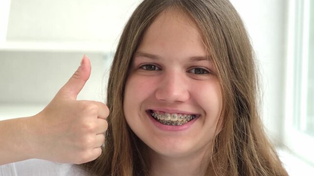 Happy smiling teenage girl with dental braces giving thumbs up. Orthodontic treatment concept