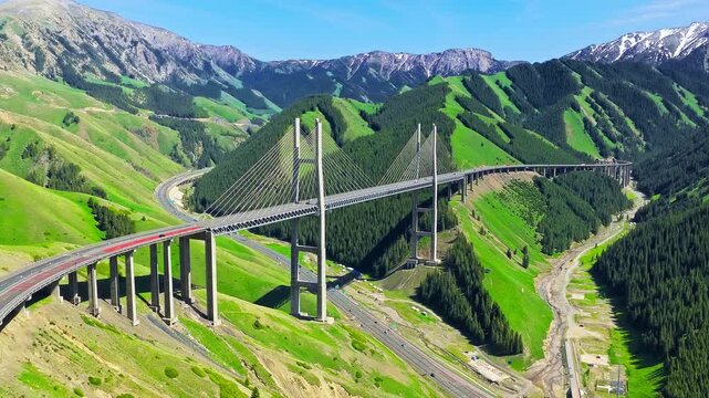Aerial view of Guozigou Bridge curving through lush green mountains and deep valleys in Xinjiang, China.