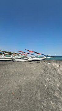 Traditional Indonesian fishing boats on black volcanic sand beach under clear blue sky.