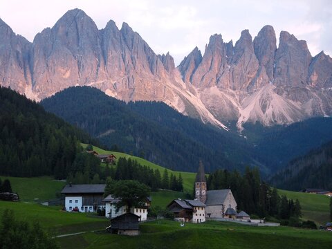 Сhiesa di Santa Maddalena with dramatic Odle Mountain Group glowing in soft pink sunset light in Val di Funes, Dolomites, Italy. iconic alpine scenery and popular travel destination in italian alps.