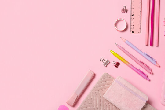 Pink office desk with various stationery items including pens ruler and notebooks on a pastel background with copy space