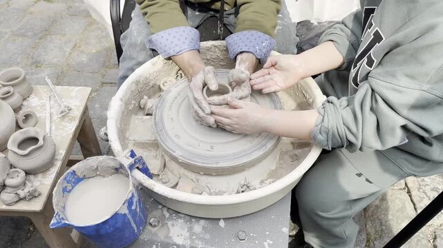 The master helps the student to create a ceramic product on a potter's wheel. Close-up of hands working with wet clay during the modeling process. The concept of craft training, traditional pottery, c