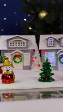 A yellow car drives up to a large Christmas village with Christmas trees and snowmen near colorful houses, and an unusual Santa Claus jumps in