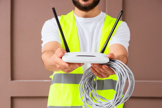 Technician in safety vest holding a white wireless router and coiled ethernet cables for Internet installation