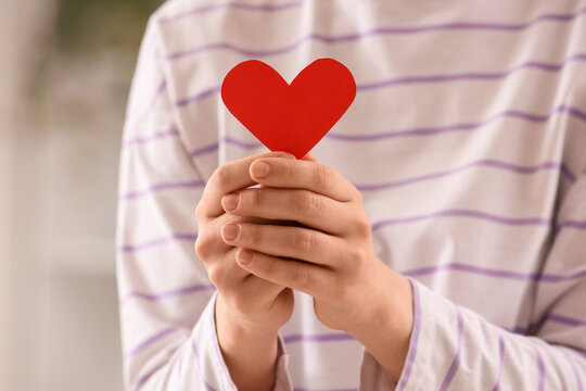 Person holding a red paper heart, love and care concept, charity and donation, health and wellness