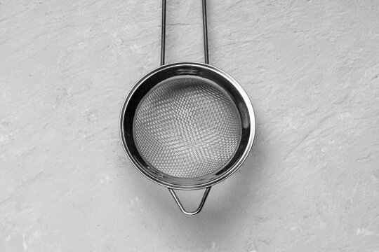 Stainless steel tea strainer with fine mesh on a textured gray background, kitchen utensil for sifting and brewing