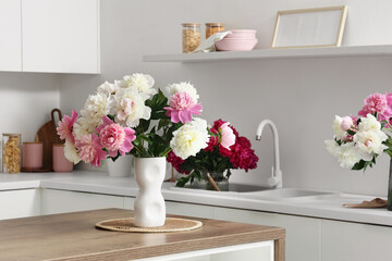 Obraz premium Pink and white peony flowers in a modern white vase on a wooden kitchen island with a clean minimalist background