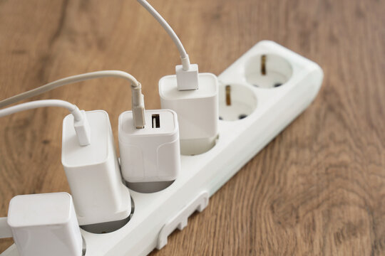 White power strip with multiple usb chargers and cables plugged in on a wooden table, energy consumption and modern technology
